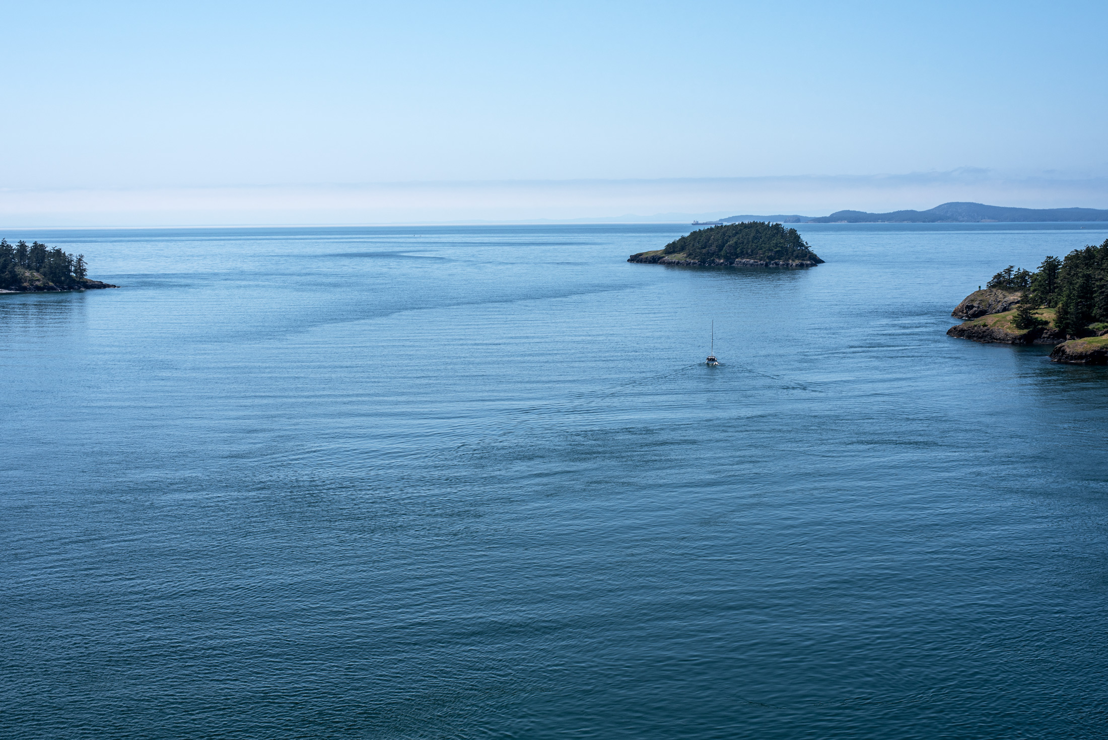 Sound and Stillness — A lone sailboat slips past a small island in the blue water off Whidbey Island, Washington.